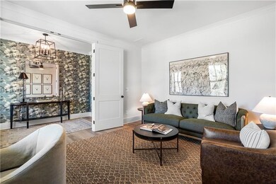 Living area with ornamental molding, wood finished floors, wallpapered walls, baseboards, and ceiling fan