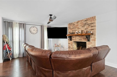 Living room with wood finished floors, ceiling fan, and a brick fireplace
