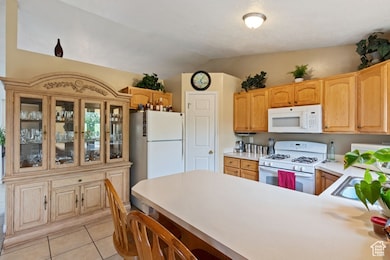 Kitchen featuring a sink, light tile patterned floors, a peninsula, lofted ceiling, and white appliances