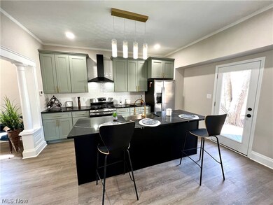 Kitchen with decorative light fixtures, wall chimney range hood, light hardwood / wood-style flooring, appliances with stainless steel finishes, and backsplash