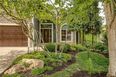 View of front of property featuring stone siding, an attached garage, and driveway