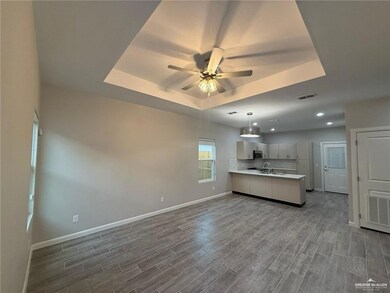 Kitchen with light countertops, a tray ceiling, dark wood-style flooring, a ceiling fan, and a peninsula
