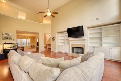 Living area with a high ceiling, a fireplace, wood finished floors, a chandelier, and ceiling fan