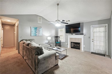 Living room featuring a tile fireplace, lofted ceiling, light carpet, and ceiling fan