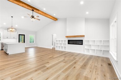 Unfurnished living room featuring ceiling fan with notable chandelier, vaulted ceiling with beams, a fireplace, and light hardwood / wood-style flooring