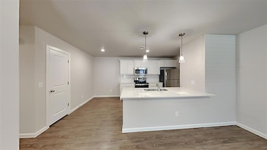 Kitchen with white cabinetry, backsplash, appliances with stainless steel finishes, dark wood finished floors, and a peninsula
