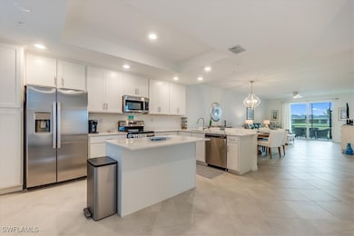 Kitchen with a raised ceiling, kitchen peninsula, decorative light fixtures, a kitchen island, and appliances with stainless steel finishes