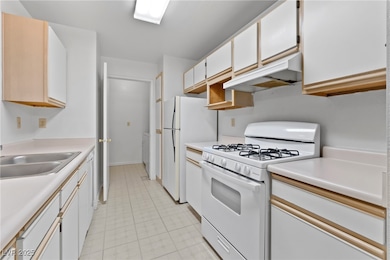 Kitchen featuring white appliances, under cabinet range hood, light countertops, and white cabinetry