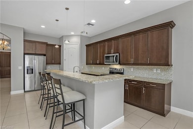 Kitchen featuring tasteful backsplash, appliances with stainless steel finishes, a breakfast bar, dark brown cabinetry, and recessed lighting