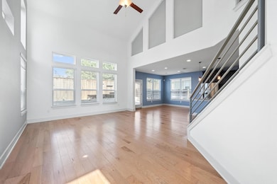 Unfurnished living room featuring a towering ceiling, stairs, light wood-style flooring, and a ceiling fan