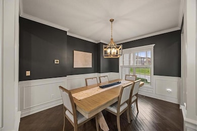 Dining area featuring ornamental molding, dark wood-style floors, a wainscoted wall, a chandelier, and a decorative wall