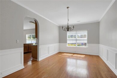 Dining area featuring arched walkways, ornamental molding, light wood finished floors, wainscoting, and a chandelier