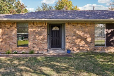 Property entrance with a shingled roof, brick siding, and a lawn