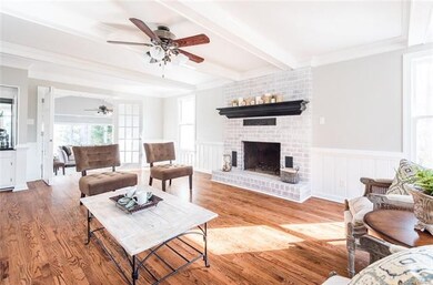 Beautiful living room featuring a brick fireplace, coffered ceiling, oak floors, wainscotting, crown molding and ceiling fan and French doors lead you out into the large family room.