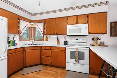 Kitchen featuring white appliances, a sink, light countertops, and light wood-style floors