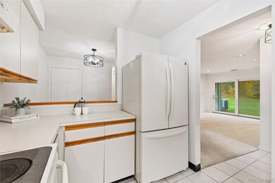 Kitchen featuring white cabinets, freestanding refrigerator, light carpet, range with electric stovetop, and light countertops