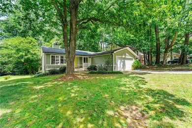 Single story home featuring a chimney, concrete driveway, a garage, and a front yard