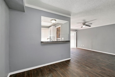 Unfurnished living room featuring a textured ceiling, dark wood finished floors, ornamental molding, and ceiling fan