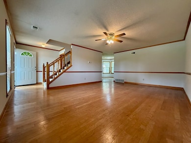 Unfurnished room featuring a ceiling fan, a textured ceiling, light wood-type flooring, stairs, and baseboards