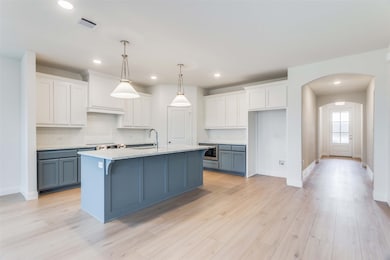 Kitchen featuring sink, white cabinetry, hanging light fixtures, an island with sink, and light hardwood / wood-style floors