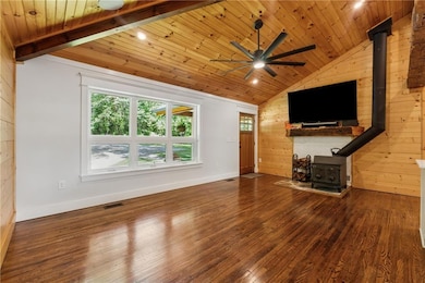 Unfurnished living room with a wood stove, wooden walls, vaulted ceiling, wood ceiling, and wood finished floors