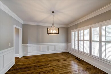 Spare room with healthy amount of natural light, a chandelier, crown molding, dark wood-style floors, and wainscoting