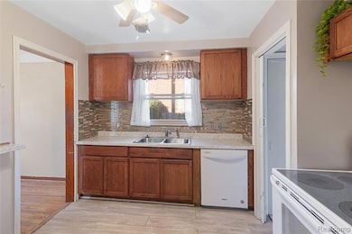 Kitchen with brown cabinetry, white appliances, light countertops, and backsplash