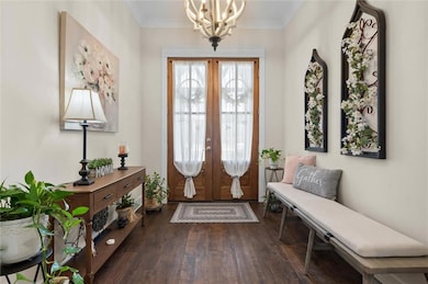 Entrance foyer with french doors, dark wood finished floors, a chandelier, and ornamental molding