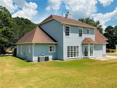 Back of house featuring a lawn, a patio, a chimney, and a shingled roof