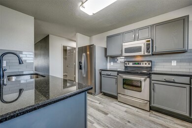 Kitchen featuring dark stone counters, light hardwood / wood-style floors, sink, backsplash, and appliances with stainless steel finishes