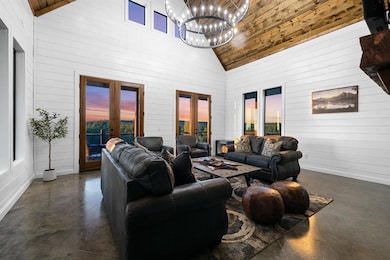 Living room with finished concrete floors, french doors, high vaulted ceiling, wood walls, and a chandelier