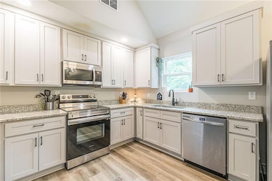 Kitchen featuring stainless steel appliances, lofted ceiling, light wood-style flooring, light stone counters, and recessed lighting