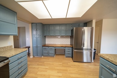 Kitchen with stainless steel appliances, light countertops, tasteful backsplash, built in desk, and light wood-type flooring