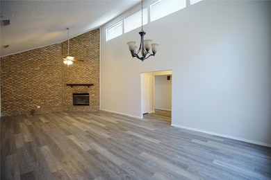 Unfurnished living room with brick wall, high vaulted ceiling, a fireplace, wood finished floors, and a chandelier