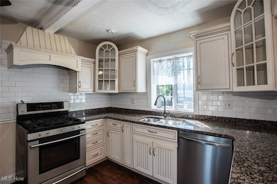 Kitchen with glass insert cabinets, appliances with stainless steel finishes, dark stone counters, decorative backsplash, and a textured ceiling