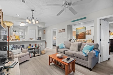 Living room featuring light wood-style floors, a ceiling fan, recessed lighting, a textured ceiling, and arched walkways