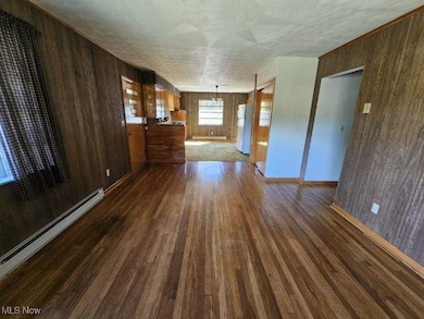 Unfurnished living room featuring wood walls, dark wood-style flooring, and a baseboard radiator