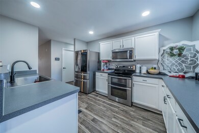 Kitchen featuring appliances with stainless steel finishes, white cabinets, dark countertops, wood finished floors, and recessed lighting