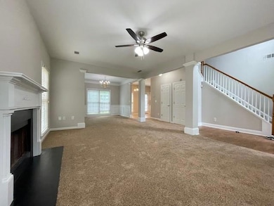 Unfurnished living room with ceiling fan, carpet, and stairway