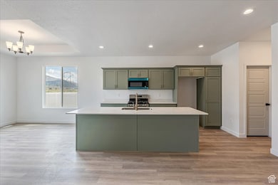 Kitchen featuring an island with sink, recessed lighting, appliances with stainless steel finishes, light wood finished floors, and green cabinets