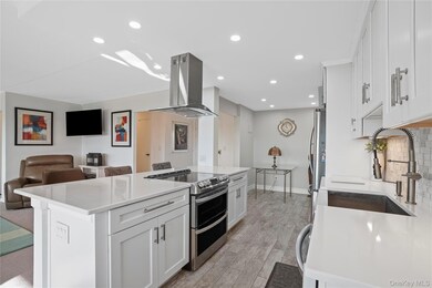 Kitchen featuring white cabinets, appliances with stainless steel finishes, open floor plan, light stone counters, and island exhaust hood