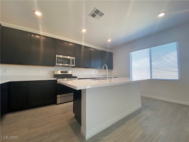 Kitchen featuring dark cabinets, stainless steel appliances, light wood-style floors, a kitchen island with sink, and recessed lighting