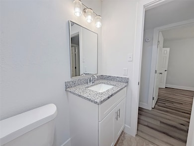 This bathroom features a modern design with a granite countertop, white vanity, and sleek fixtures. There's a large mirror and stylish lighting above. The neutral color palette and wood-look flooring create a clean, inviting space.