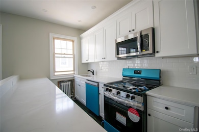 Kitchen with stainless steel appliances, tasteful backsplash, white cabinetry, and radiator heating unit