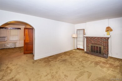 Unfurnished living room with light carpet, a brick fireplace, and radiator heating unit