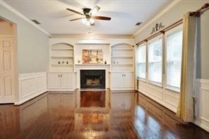 Unfurnished living room with a decorative wall, a wainscoted wall, ornamental molding, a fireplace, and dark wood finished floors