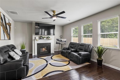 Living room featuring hardwood flooring, flooded by natural light; baseboards, ceiling fan, and a fireplace with flush hearth make the room cozy and complete