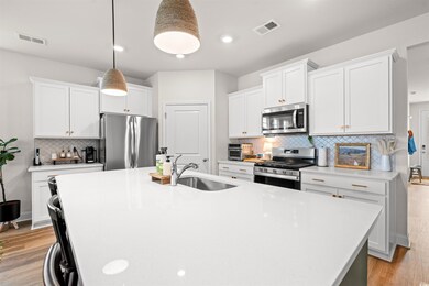 Kitchen featuring appliances with stainless steel finishes, a sink, decorative backsplash, a center island with sink, and light countertops
