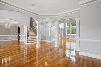 Unfurnished living room with light wood finished floors, arched walkways, ornamental molding, a decorative wall, and a wainscoted wall