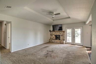 Unfurnished living room with a raised ceiling, a ceiling fan, carpet flooring, a brick fireplace, and french doors